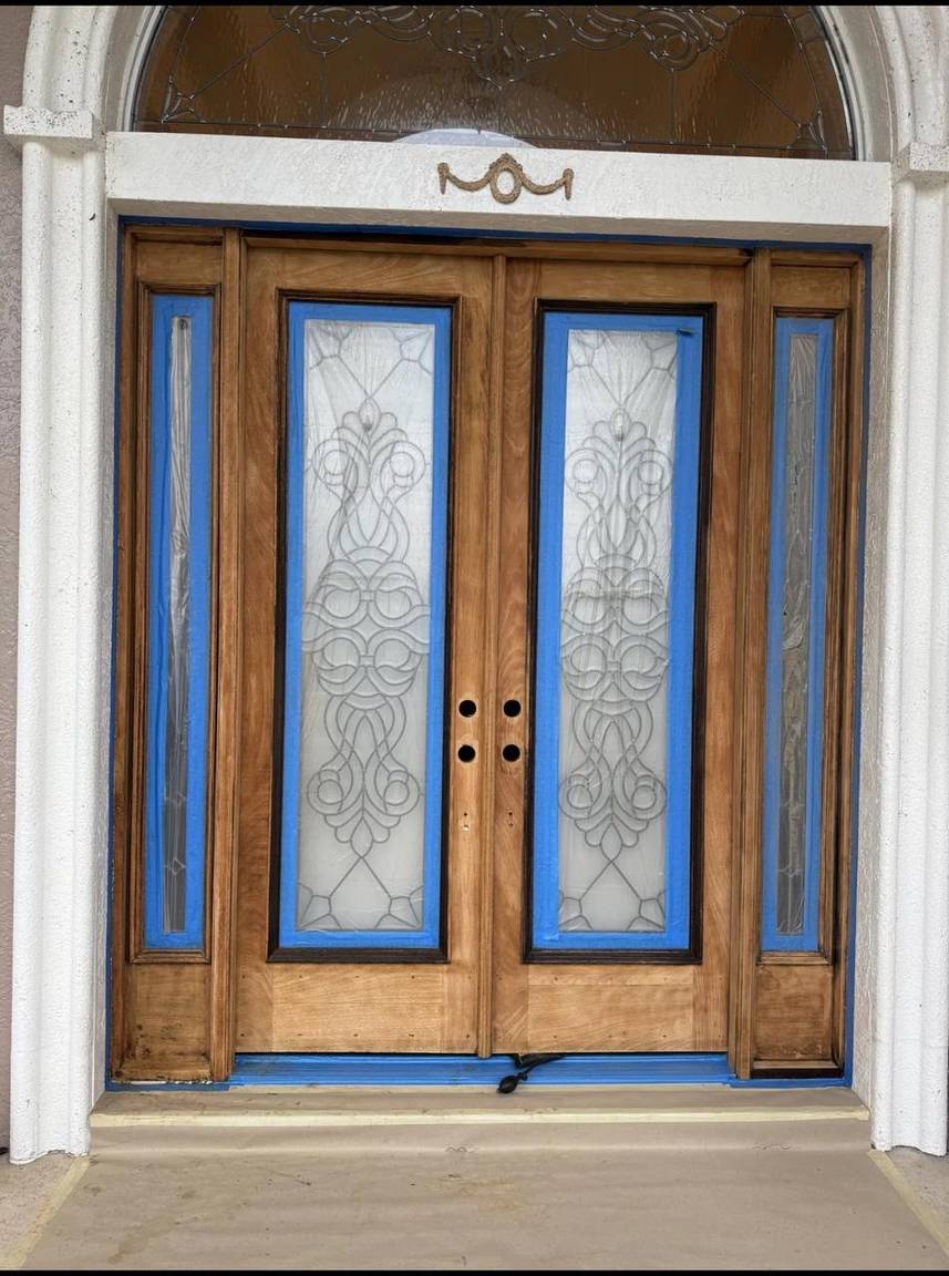 Entry doors stripped to bare wood with glass masked in blue tape during refinishing